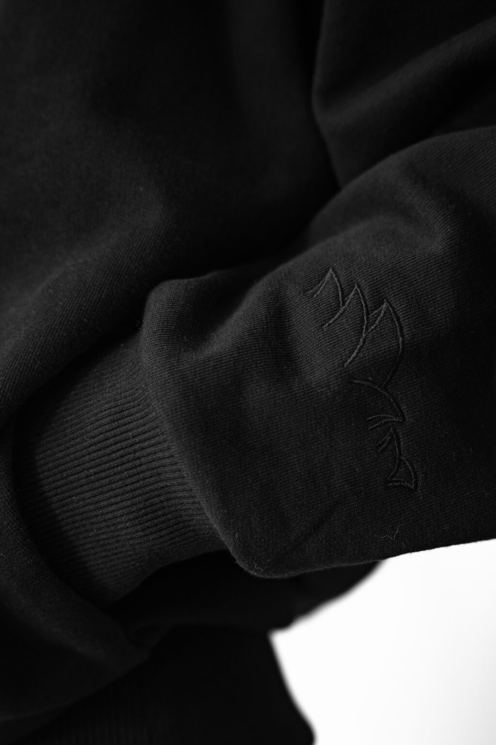 Close-up of a black sweatshirt sleeve with subtle embroidery of a stylized design of the Opera House in Sydney. The fabric appears soft, conveying a sense of warmth and comfort