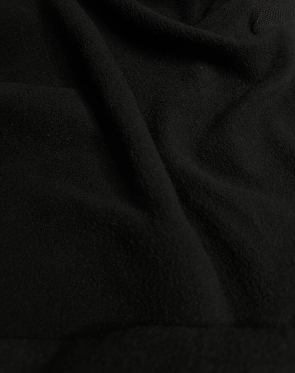 Close-up of a dark, soft fabric with subtle folds ans a plush texture, creating a sens of warmth and comfort through its rich appearance.